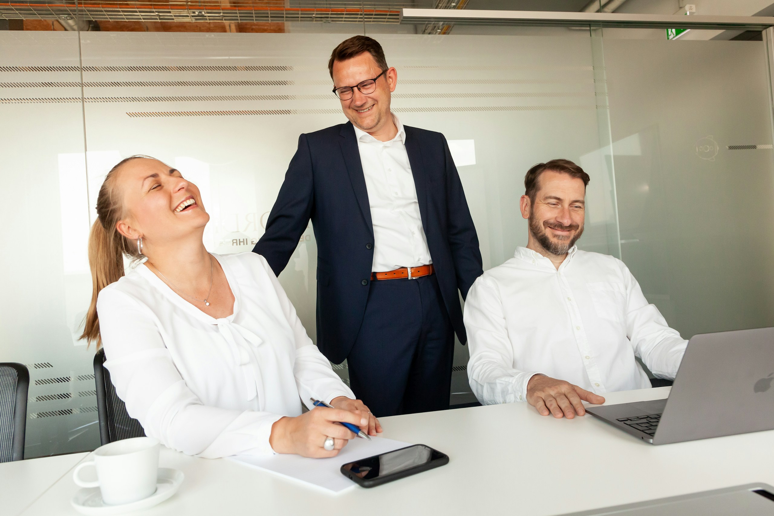 Three colleagues laughing together in a bright office